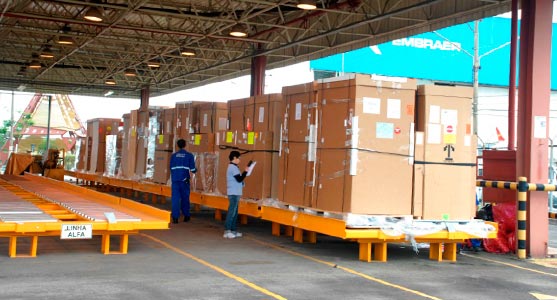 Processo de movimentação de volumes no terminal de logística de carga de São José dos Campos. Na imagem, um funcionário faz anotações em uma planilha enquanto outro monitora as cargas distribuídas em paleteiras.